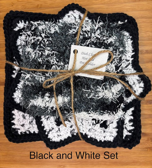 Three-piece handmade crocheted kitchen set in black, white, and gray, featuring a swirling star-shaped hot pad, a thick striped square potholder, and a textured fuzzy square dish scrubby.